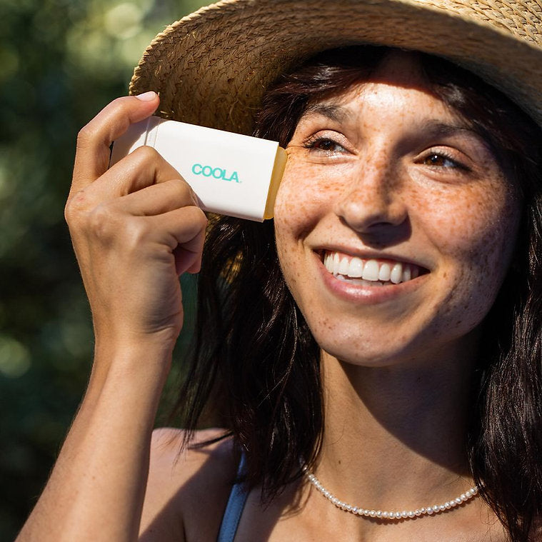 Woman applying Classic Organic Sunscreen Stick SPF 30, Tropical Coconut scent, for broad-spectrum protection outdoors.