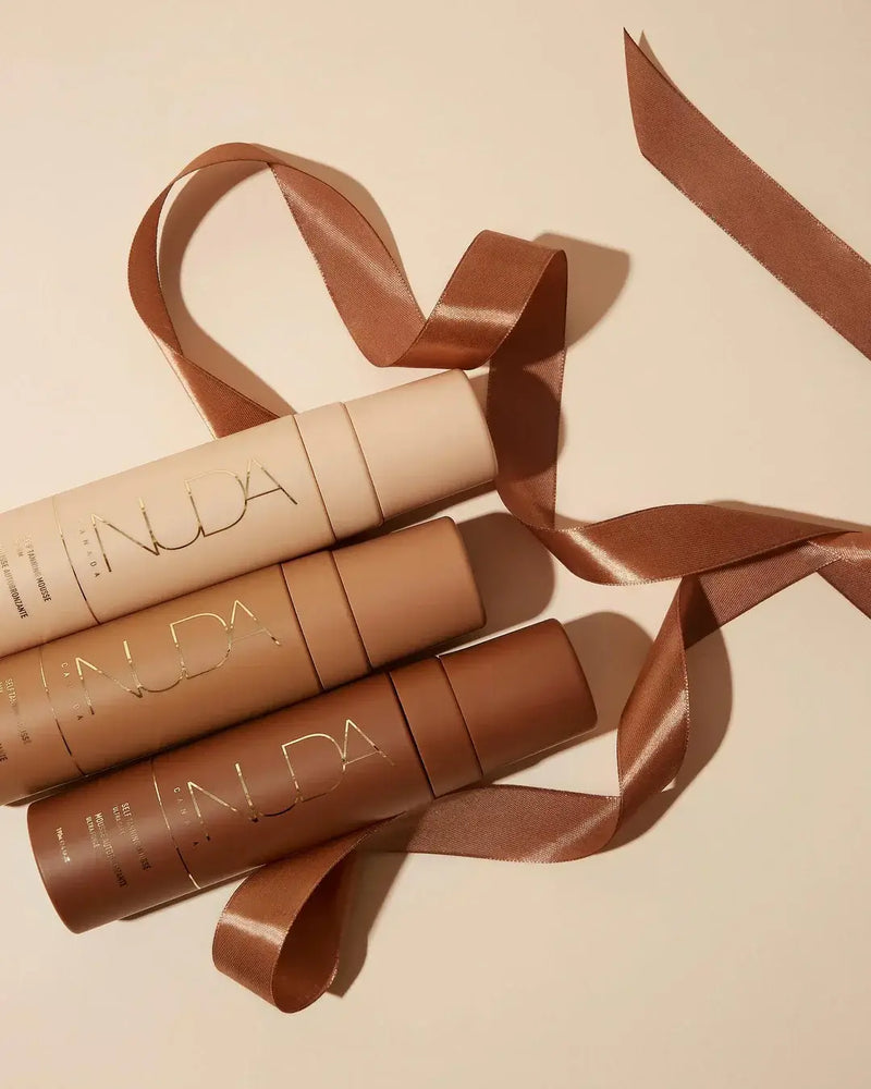 Three nude-toned cosmetic bottles with brown ribbon on neutral background