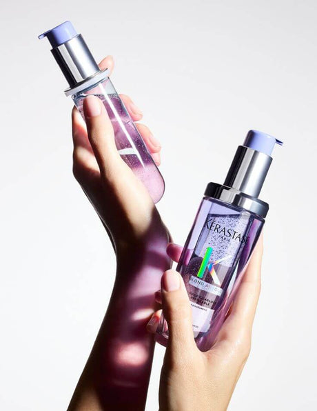 Hands holding Kerastase hair products with pump dispensers on a white background.