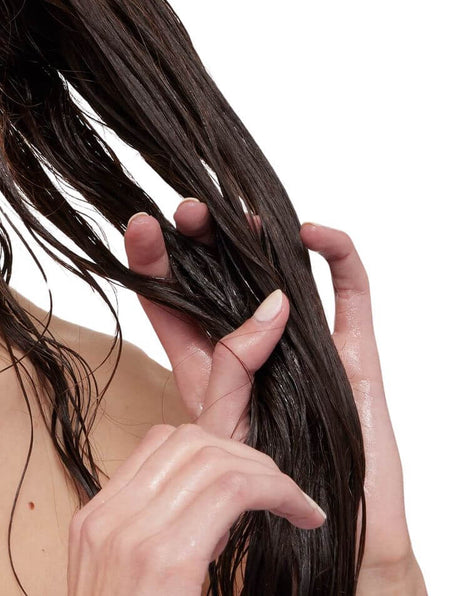 Person gently detangling wet, long hair with fingers on a white background.