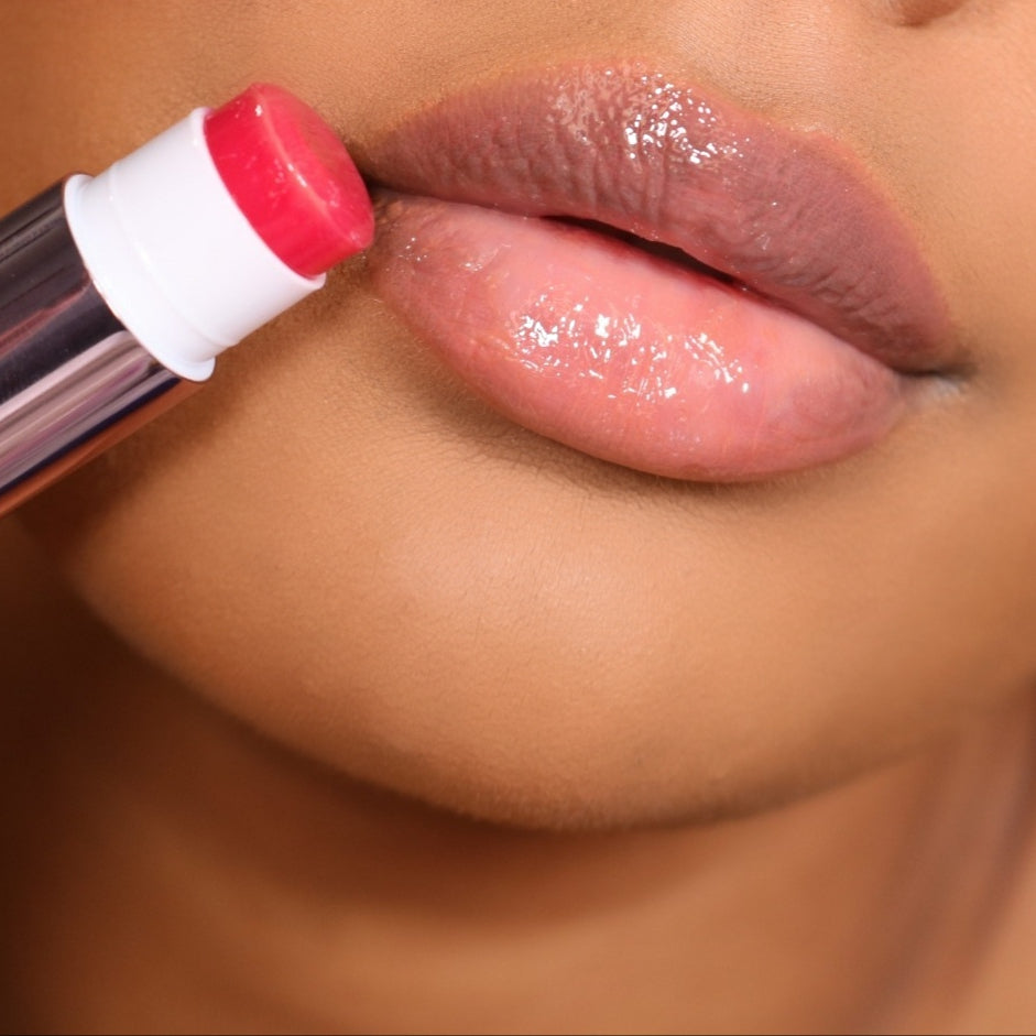 Jello Gloss Balm being applied to lips, moisturizing with Vitamin E and Avocado Oil for a glossy, non-sticky finish with pink lemonade scent.