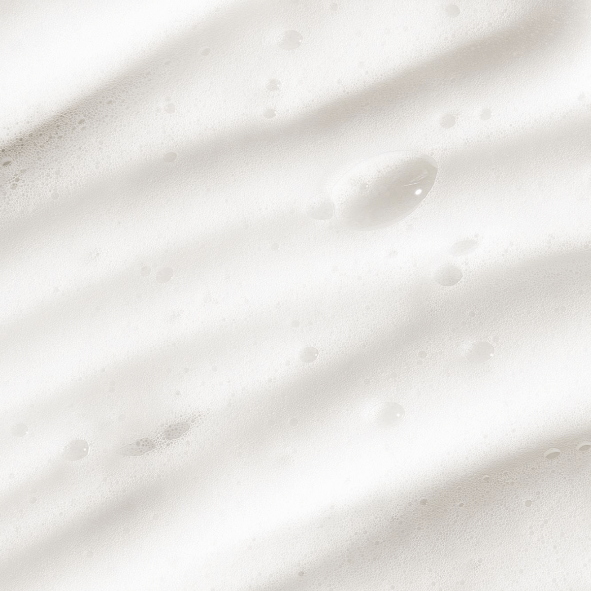 Close-up view of white foamy mousse texture, representing Sunless Tan Remover exfoliating mousse with skin-nourishing ingredients.