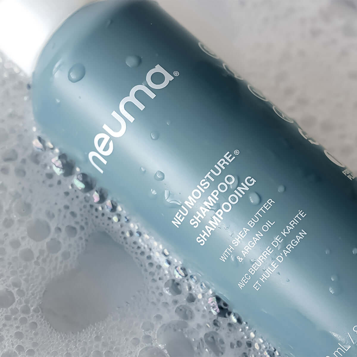Neu Moisture Shampoo bottle surrounded by rich, sudsy lather, highlighting gentle cleansing and moisture replenishment.