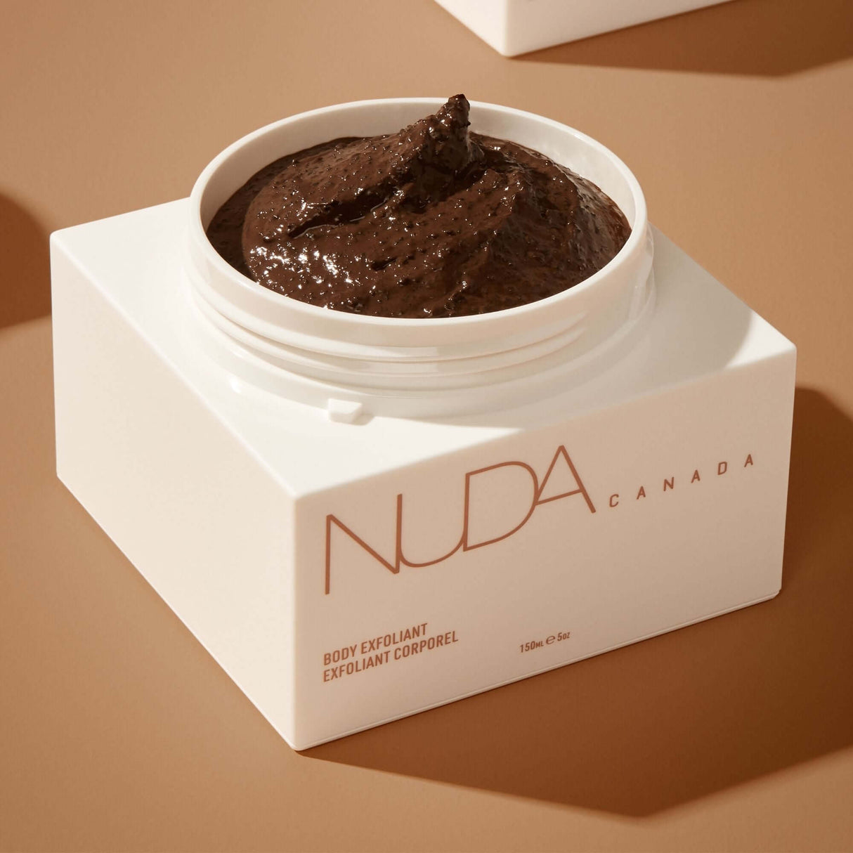 Luxurious creamy body exfoliant with Coffee Arabica in an elegant white container, enriched with coconut oil and vitamin E for smoother skin.