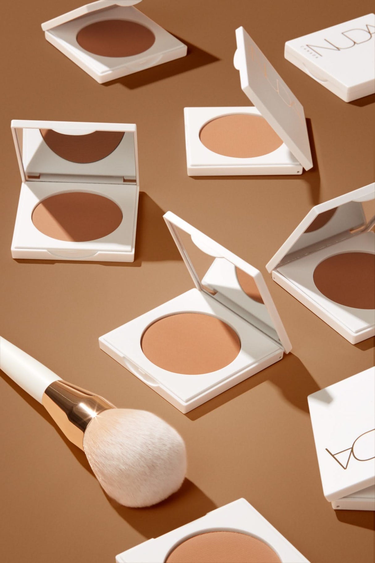 Collection of bronzing powders and a blending brush on a brown surface.
