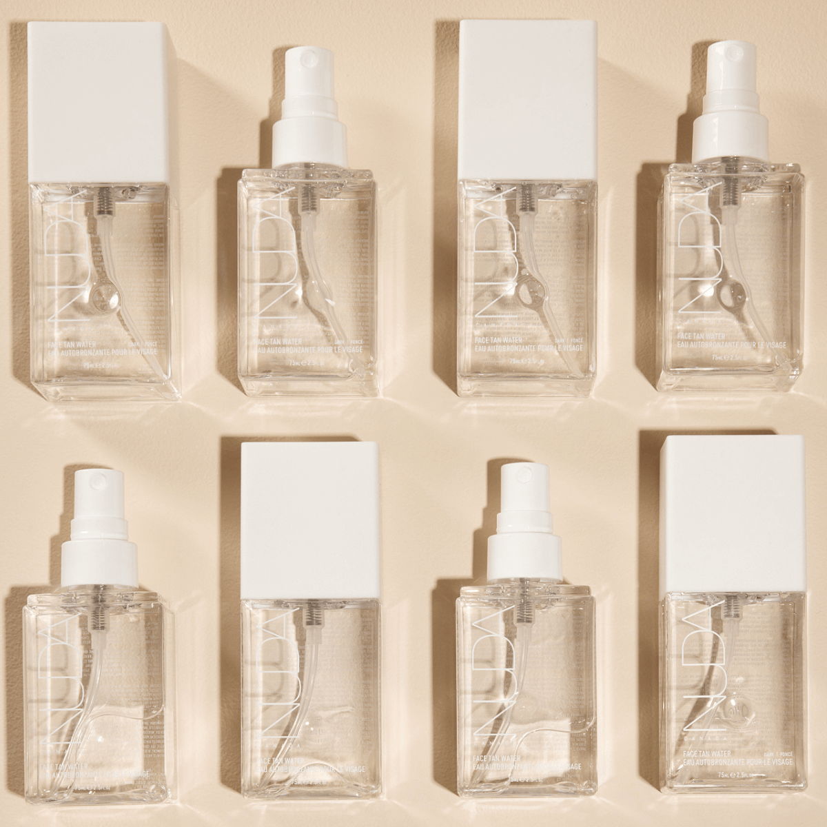 Face Tan Water bottles with white caps, arranged in a symmetrical pattern, promoting even, radiant skin with natural ingredients.