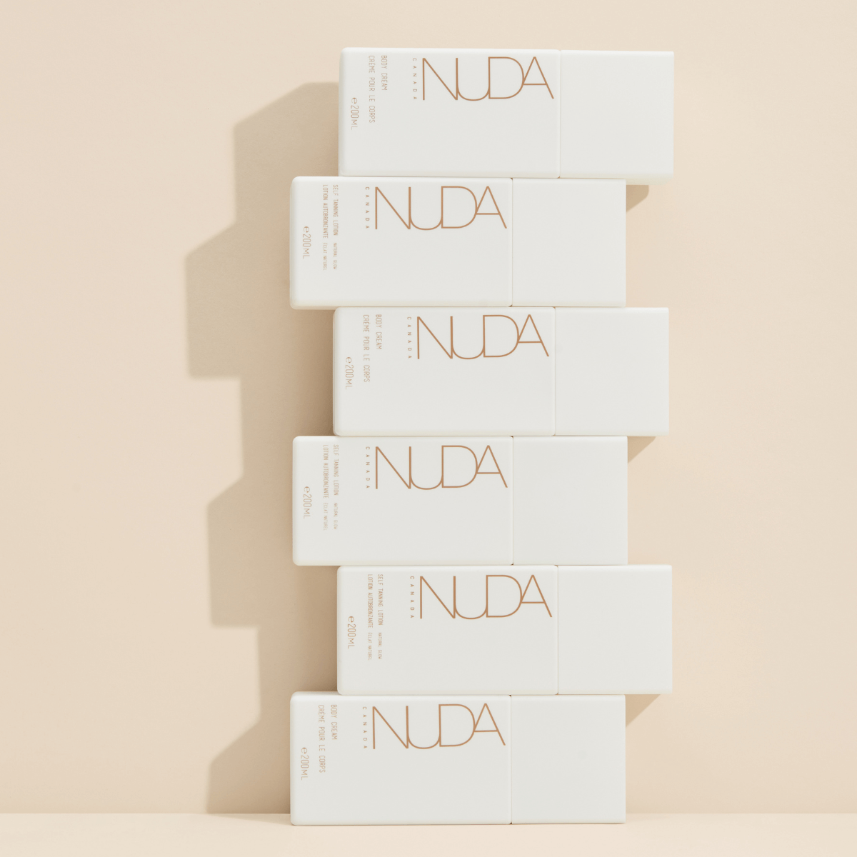Nuda self tanning lotion bottles stacked against a beige background, illustrating luxurious skincare product design.