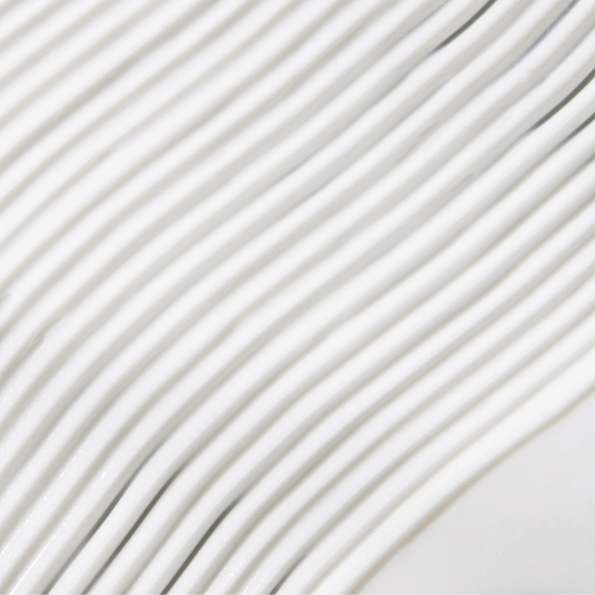 Close-up of smooth white lotion texture with wavy lines, illustrating hydrating self-tanning lotion's creamy consistency.