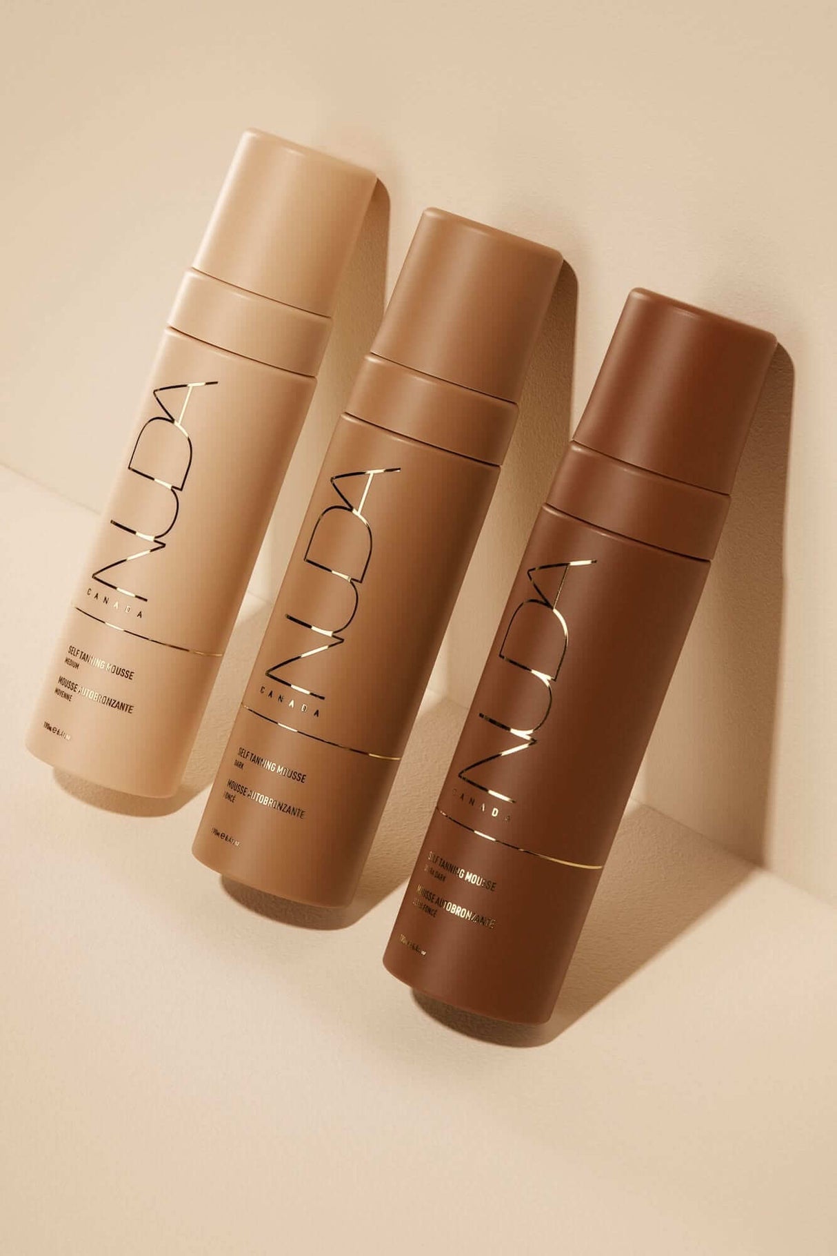 Glow Kit self tanning mousses in light, medium, and dark shades for a tailored sun-kissed tan, shown with sleek bottles on beige background.