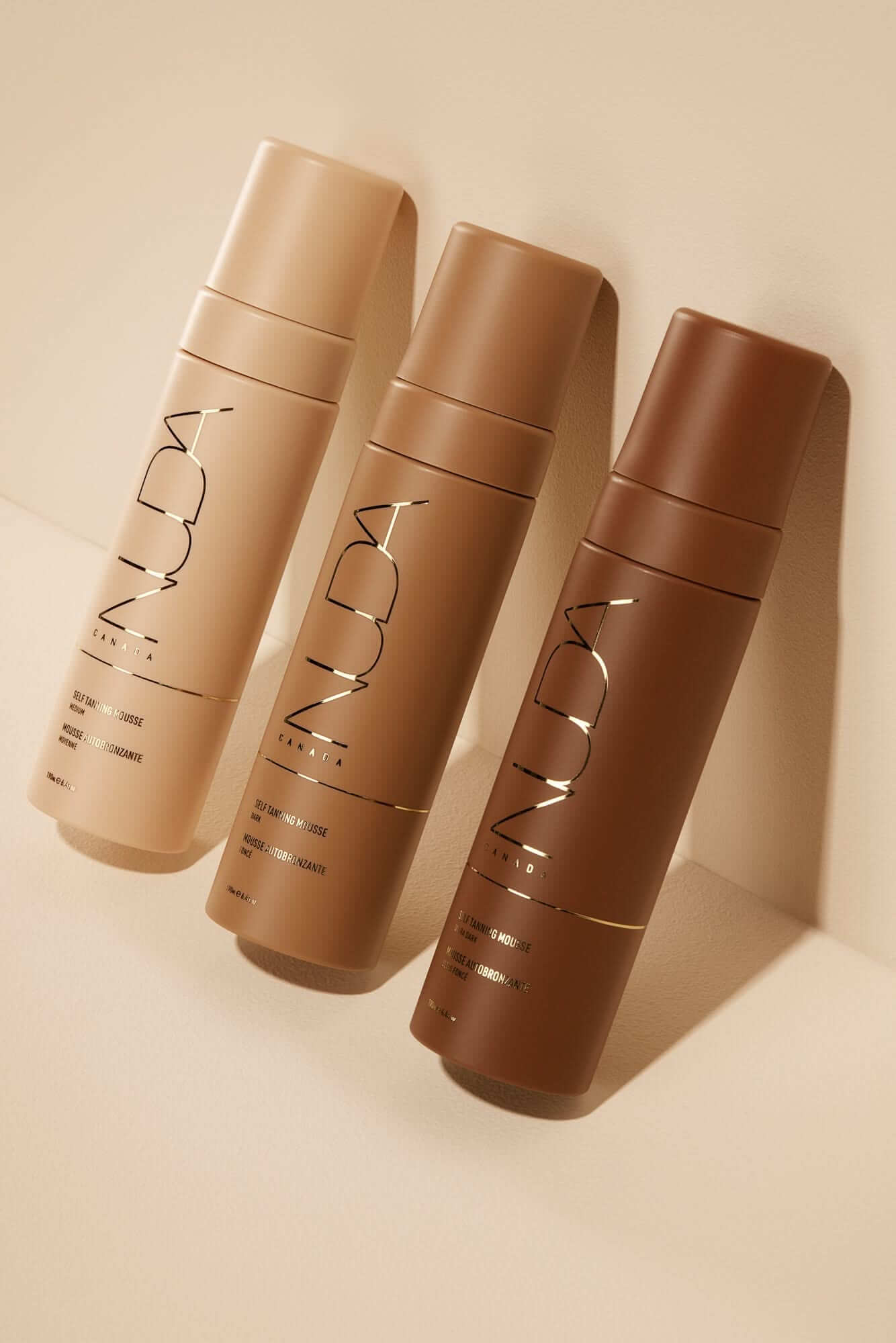 Glow Kit self tanning mousses in light, medium, and dark shades for a tailored sun-kissed tan, shown with sleek bottles on beige background.