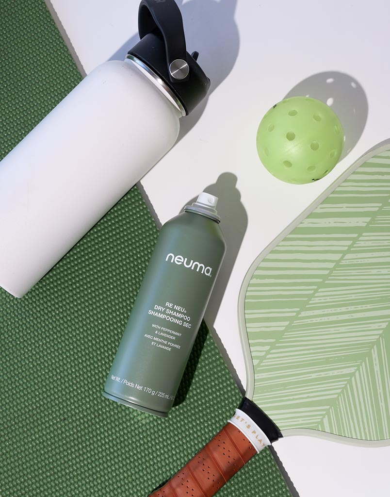 Re Neu Dry Shampoo can with water bottle, paddle, and green ball, on a green mat.