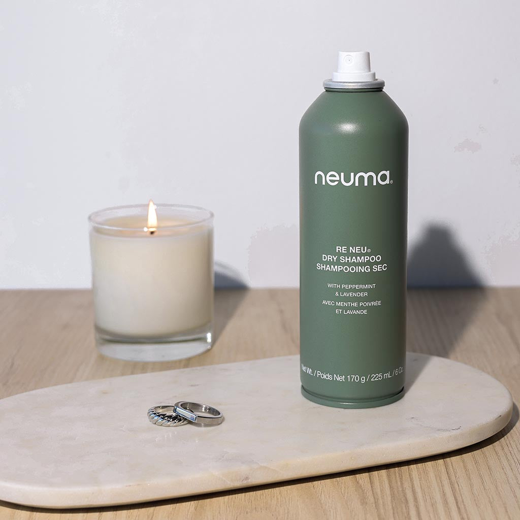 Re Neu Dry Shampoo bottle displayed on marble tray with candle.