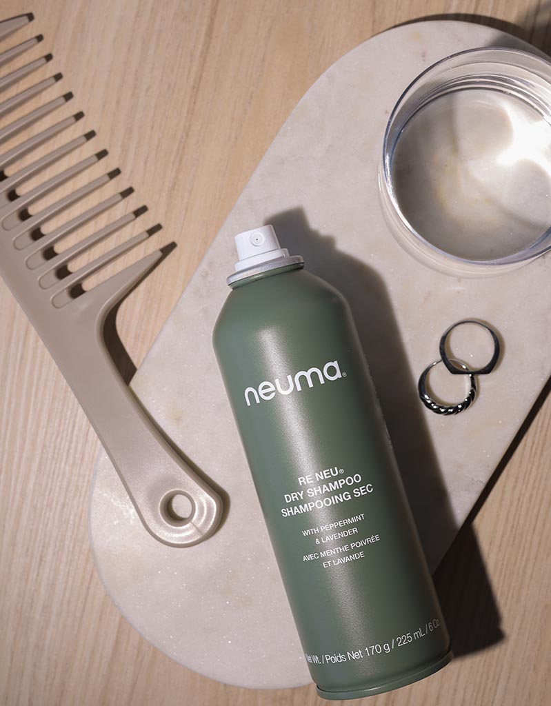 Re Neu Dry Shampoo can on a marble tray with a comb, glass, and rings, offering talc-free volume, oil absorption, and a coconut aroma.