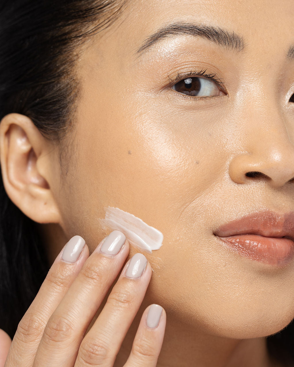 Woman applying AHA/BHA exfoliating cream to her cheek, showing skincare routine focused on smoothing and refreshing skin.