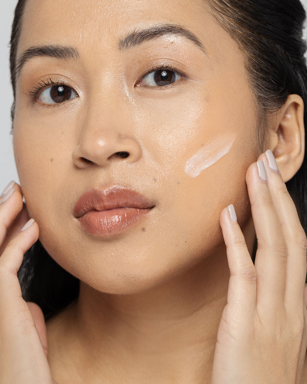 Woman applying acne treatment lotion with Benzoyl Peroxide to face for clear skin care routine.