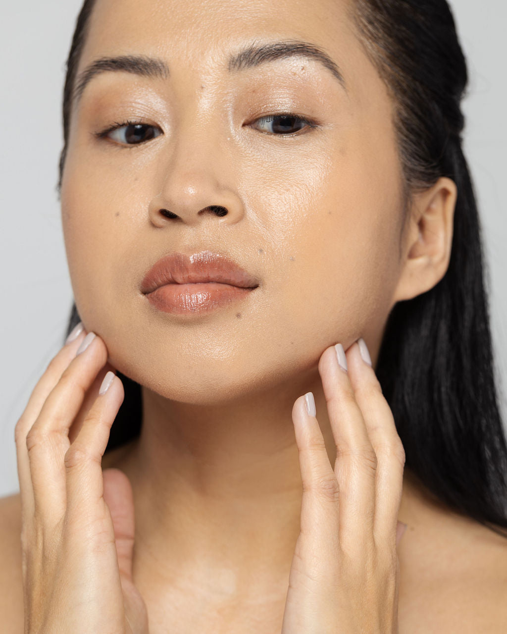 Woman gently touching her face, showcasing smooth, radiant skin after using Vivier QuintiSerum™ antioxidant serum.