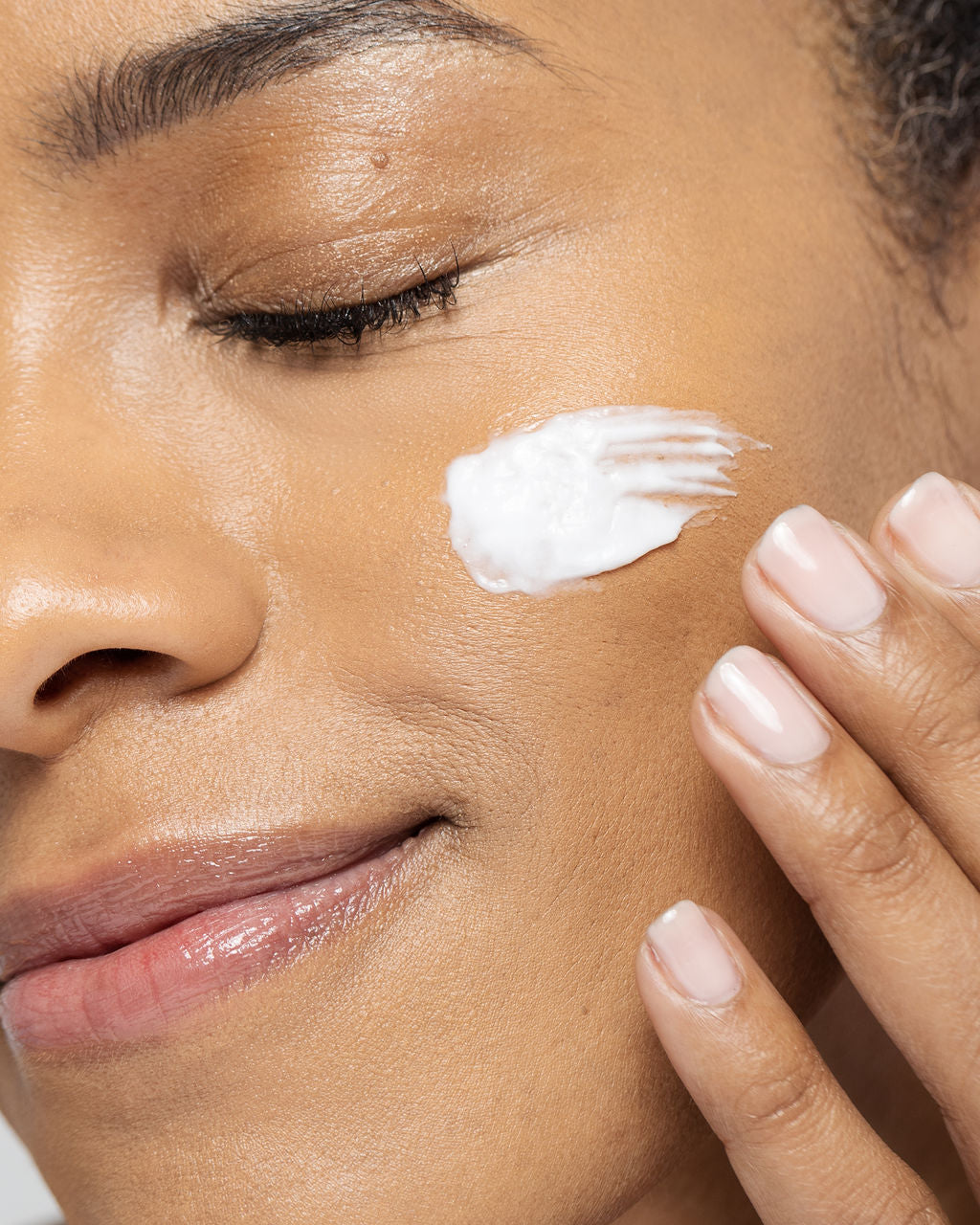 Woman applying skin brightening cream to cheek for even tone and reduced dark spots.