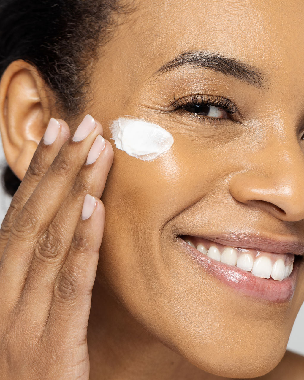 Close-up of a smiling person applying Ultra Hydrating Mask, highlighting smooth and vibrant skin from the moisturizing formula.