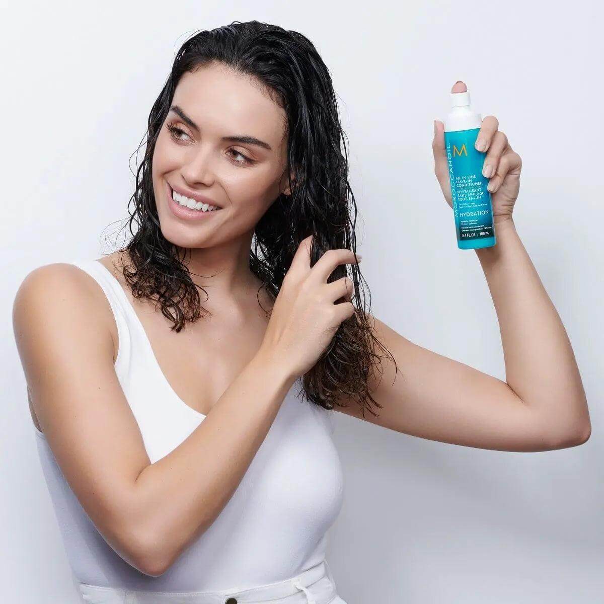 Woman applying Moroccanoil All In One Leave-in Conditioner to wet hair for hydration and shine