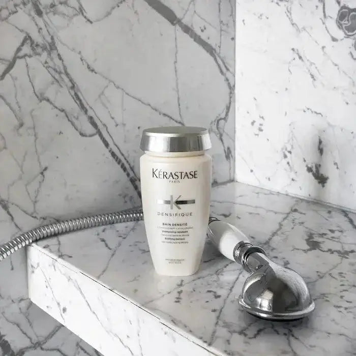 Kérastase Bain Densité shampoo bottle on marble surface, enhances hair density and thickness, ideal for fine or thinning hair.