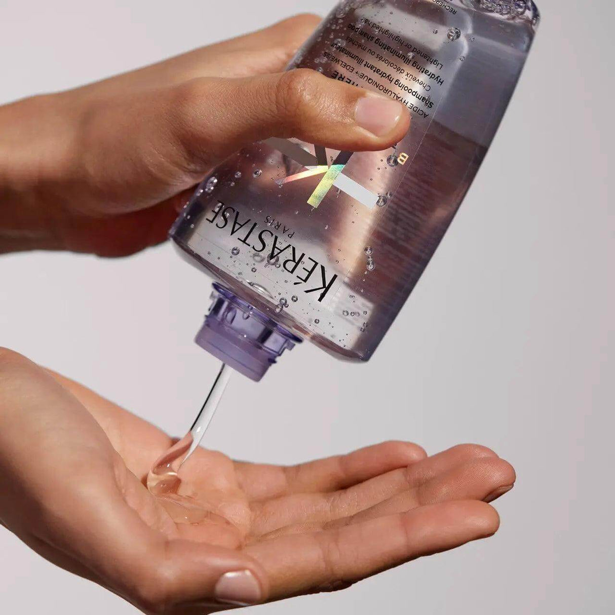 Person dispensing Kerastase Bain Lumière Blond Absolu shampoo, designed to hydrate and enhance shine for blonde hair.