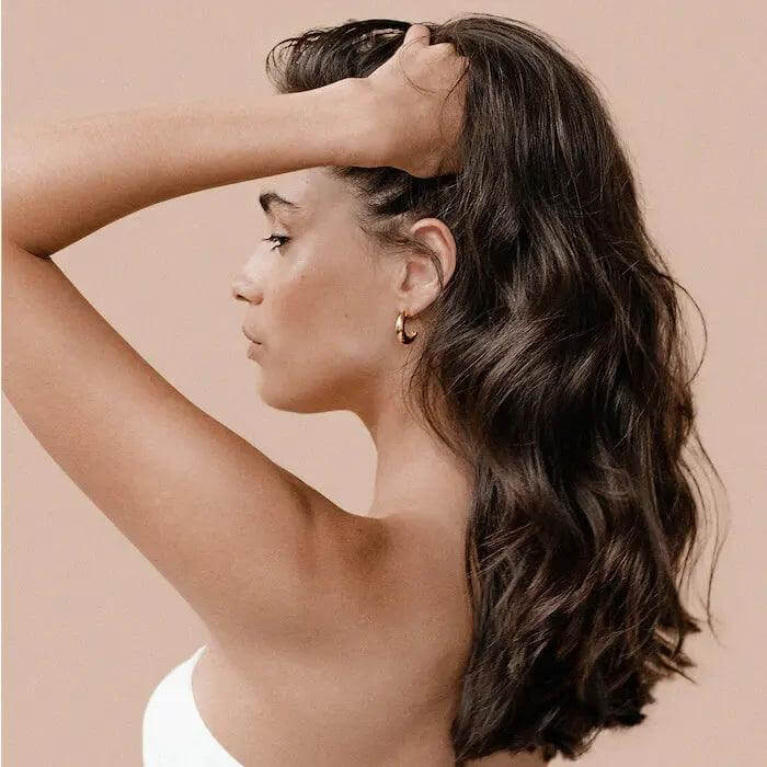 Woman with long, glossy hair showcasing results of Bain Régénérant shampoo against a neutral background.