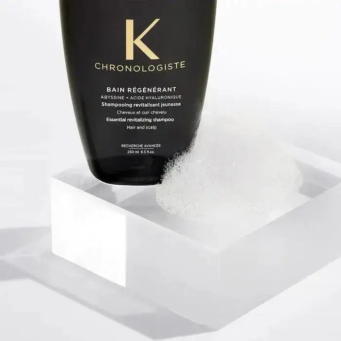 Bain Régénérant Chronologiste shampoo on a white pedestal, surrounded by bubbles, ideal for rejuvenating all hair types.