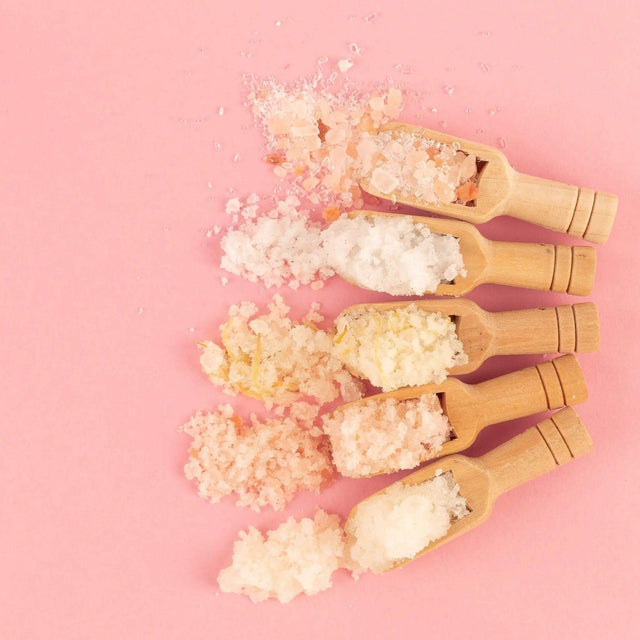 Wooden scoops with Himalayan and epsom bath salts on pink background for relaxation and toning with neroli and grapefruit scent