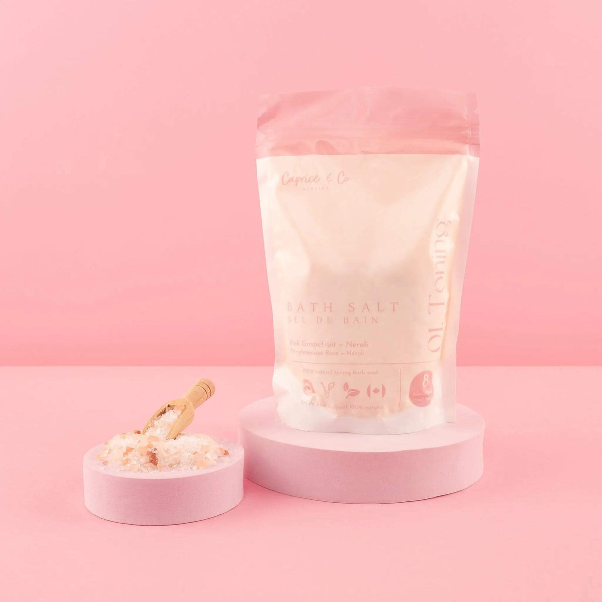All Natural Bath Salts with Neroli & Grapefruit in pink packaging on a pedestal, next to a scoop of salts.