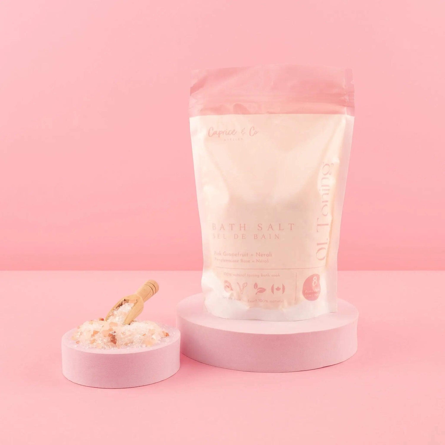 All Natural Bath Salts with Neroli & Grapefruit in pink packaging on a pedestal, next to a scoop of salts.