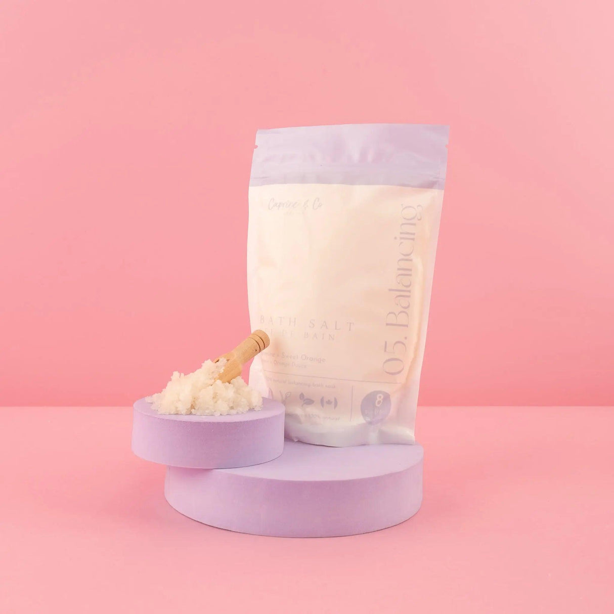 All Natural Bath Salts in Lavender Packaging with Wooden Spoon on Pink Background