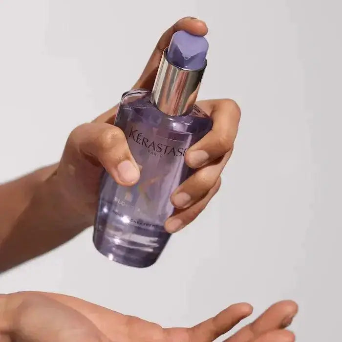 Person holding Kérastase Blond Absolu Huile Cicaextreme hair oil for damaged hair nourishment.