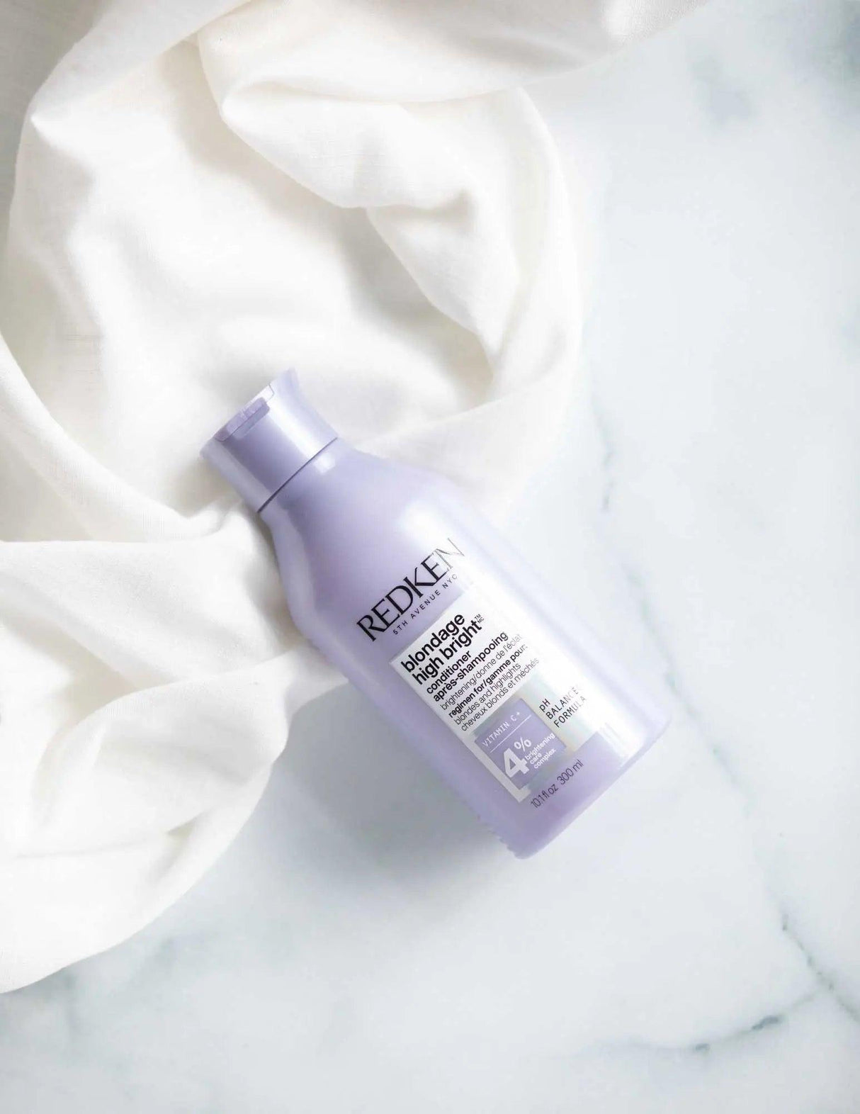 Redken Blondage High Bright Conditioner for blonde hair, enhances brightness, nourishes, and reduces brassiness on a white cloth.