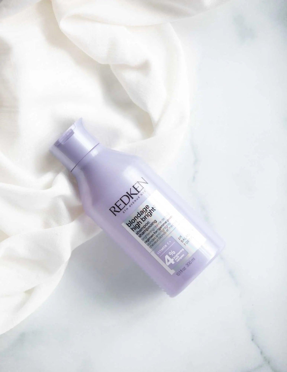 Redken Blondage High Bright Shampoo bottle for enhancing blonde hair vibrancy and reducing brassiness, on a marble surface.
