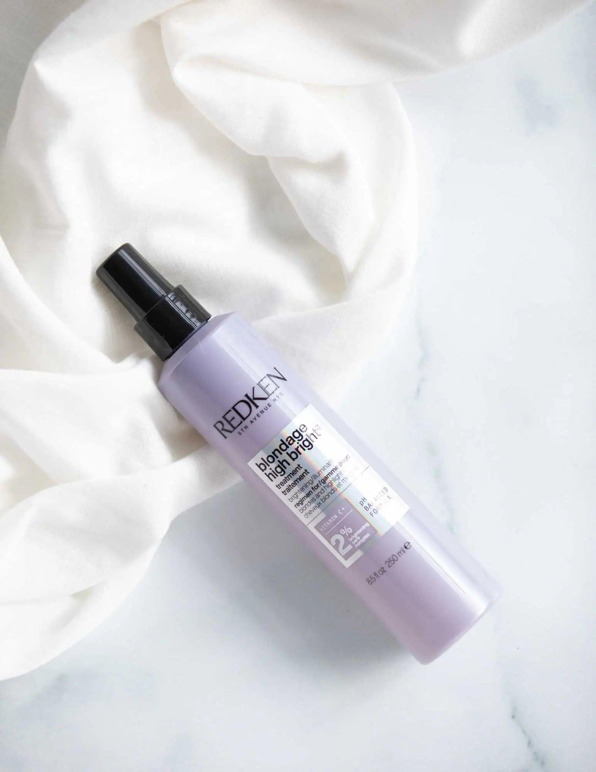 Redken Blondage High Bright Treatment bottle on soft fabric, ideal for neutralizing brassiness in blonde and highlighted hair.