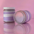Natural body scrub in bubblegum scent, enriched with organic coconut oil and shea butter, shown in two jars on a pink background.