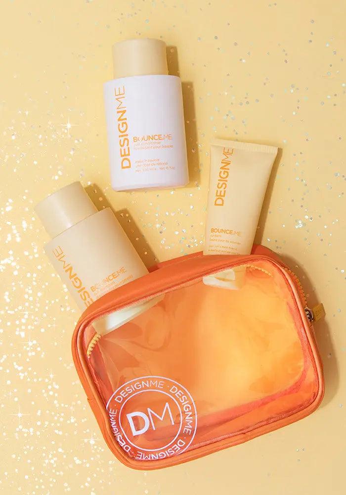DESIGNME BOUNCE.ME Curl Glitz Kit with shampoo, conditioner, curl balm, and orange travel bag on sparkling yellow background.