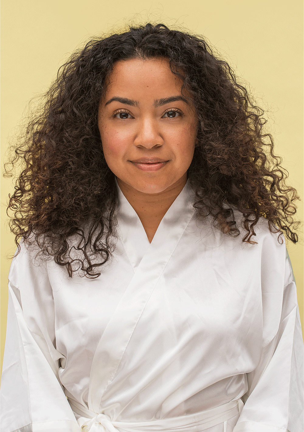 Woman with curly hair wearing a white robe against a yellow background, showcasing natural hair texture and style.