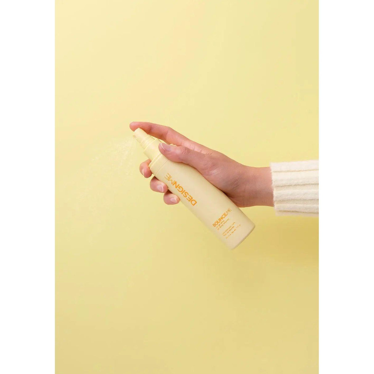 Hand holding Bounce.Me Curl Spray Gel bottle against a yellow background.