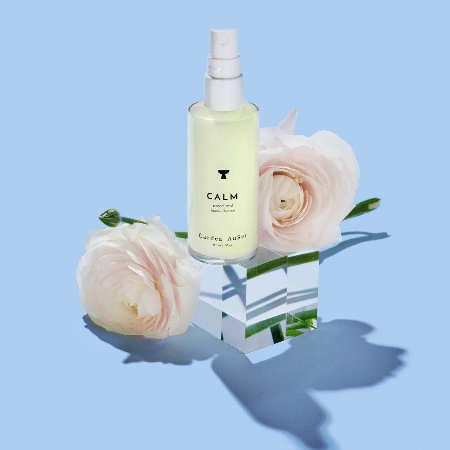 Calm Mood Mist bottle with white roses on a mirrored cube, ideal for relaxation and aromatherapy using lavender, bergamot, and frankincense.