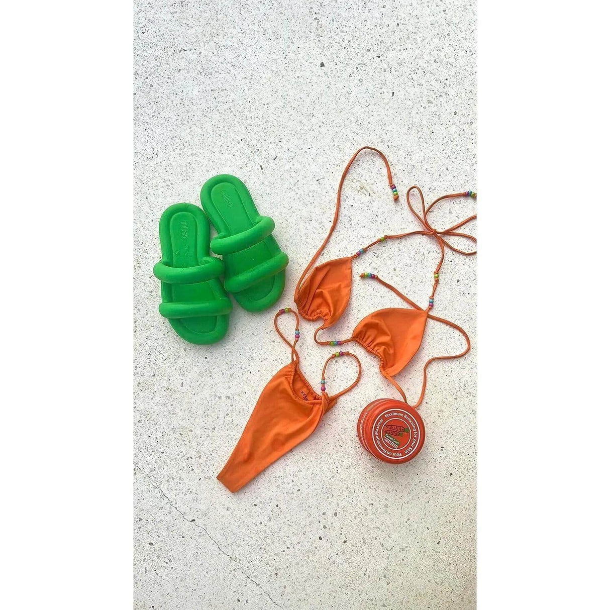 Orange bikini and carrot cream tan accelerator with green sandals on white background