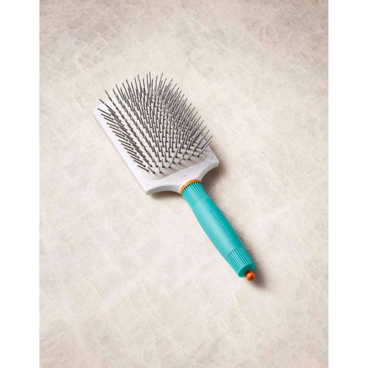 Moroccanoil Ceramic Paddle Brush with ionic properties, teal handle, and sectioning tip for smooth, shiny hair styling.