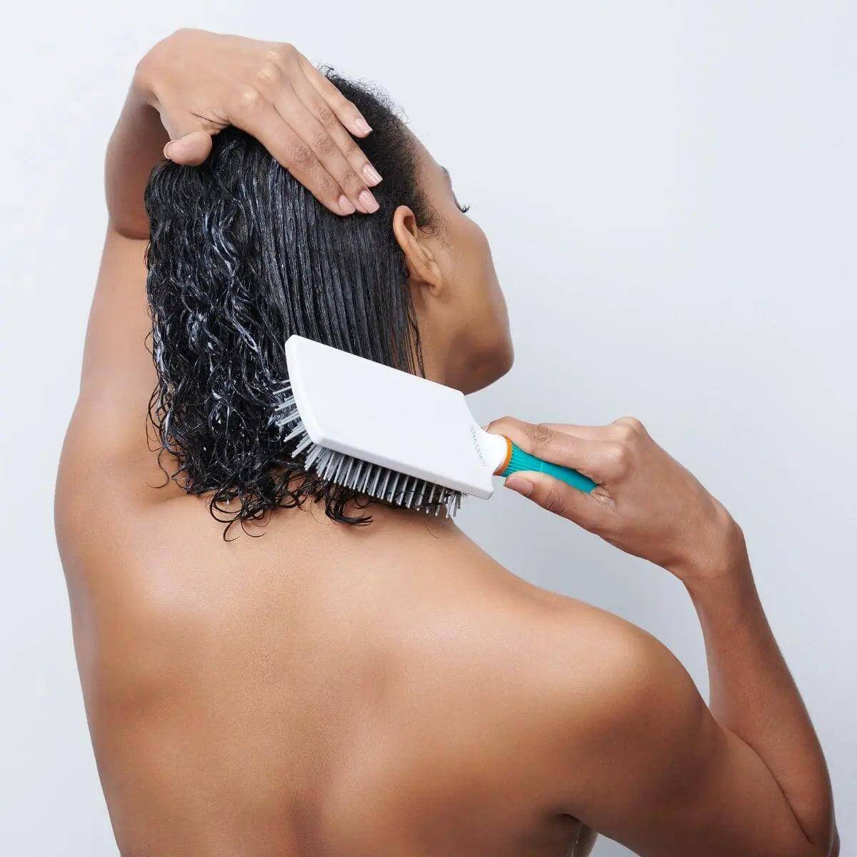 Person using Moroccanoil Ceramic Paddle Brush to style wet hair, showcasing even heat distribution for shine and quick drying.