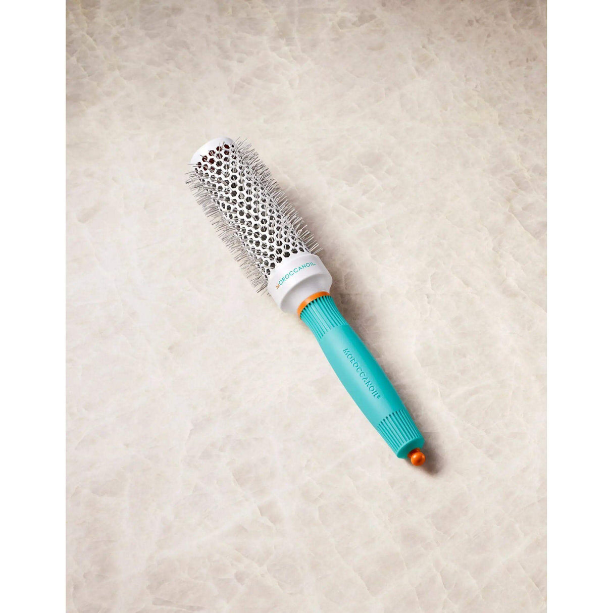 Ionic ceramic round hairbrush with retractable styling clip for faster drying, featuring turquoise handle on a marble background.