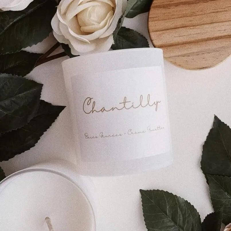 Chantilly candle with frosted berries and whipped cream scent, in a recyclable glass jar, surrounded by flowers and leaves.