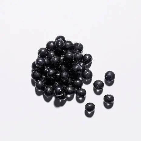 Black pearls on white background, representing Kérastase Chronologiste Sérum Universel's luxurious ingredient capsules.