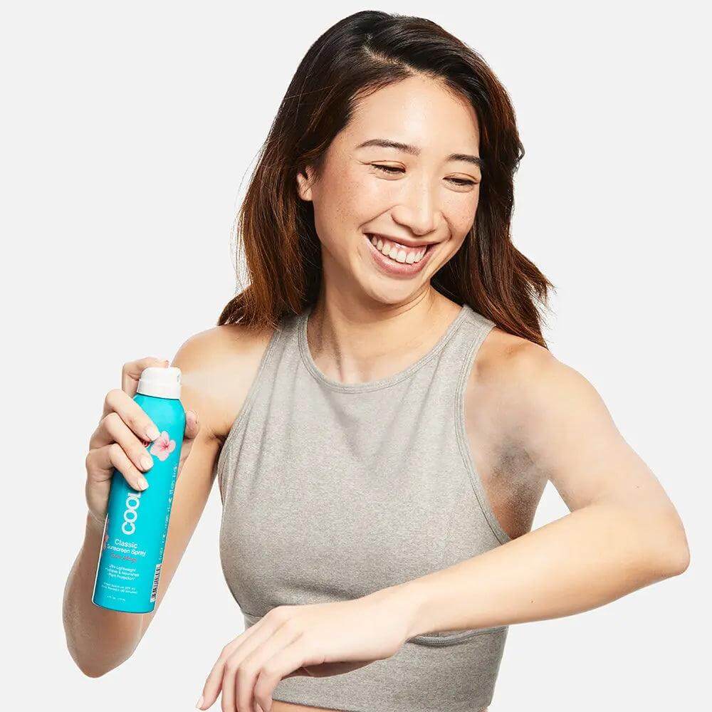 Woman applying Classic Body Organic Sunscreen Spray SPF 50 Guava Mango with a smile, showcasing skin protection benefits.