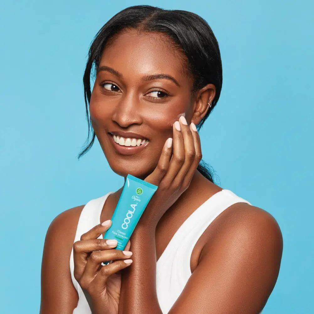 Smiling woman holding Classic Face Organic Sunscreen Lotion SPF 30 - Cucumber against blue background