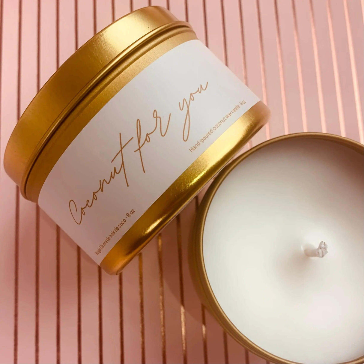 Gold tin of 'Coconut For You' candle with coconut wax blend, placed on a pink striped background.