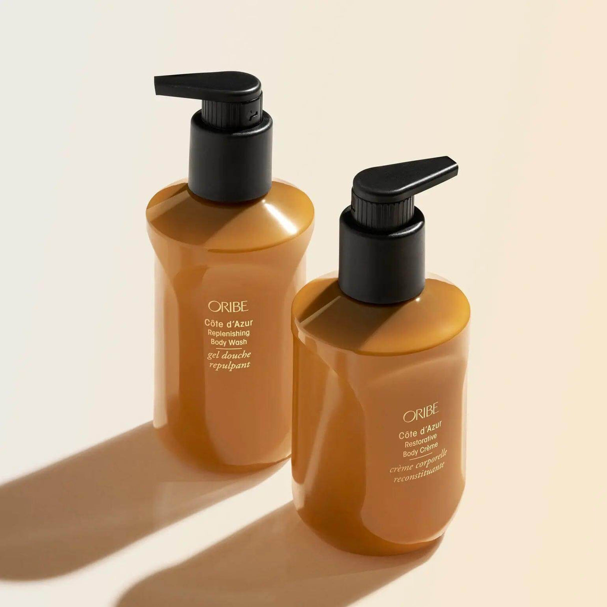ORIBE Côte d'Azur Body Crème and Body Wash bottles with black pumps in bright lighting, highlighting luxurious skincare packaging.
